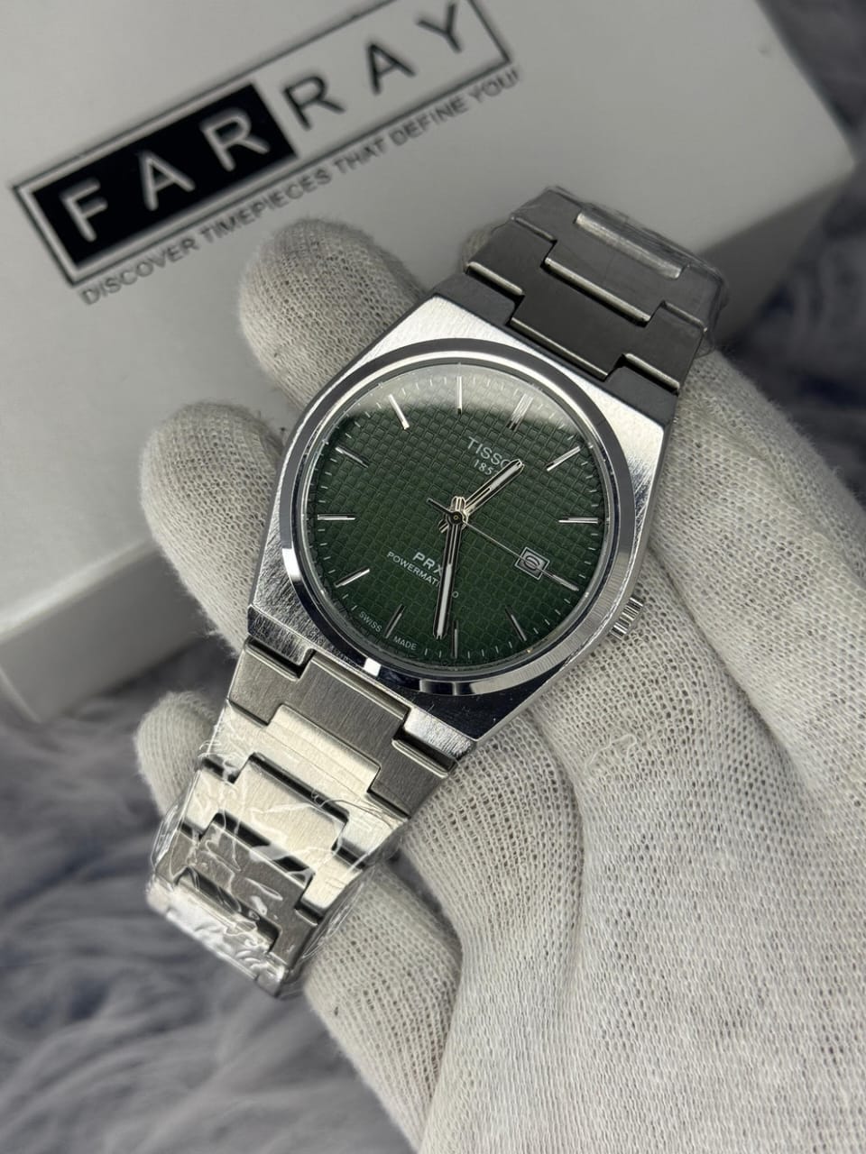 Silver watch with green face held by a gloved hand against a gray background